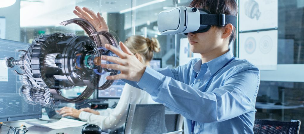 Computer Science Engineer wearing Virtual Reality Headset Works with 3D Model Hologram Visualization, Makes Gestures. In the Background Engineering Bureau with Busy Coworkers.